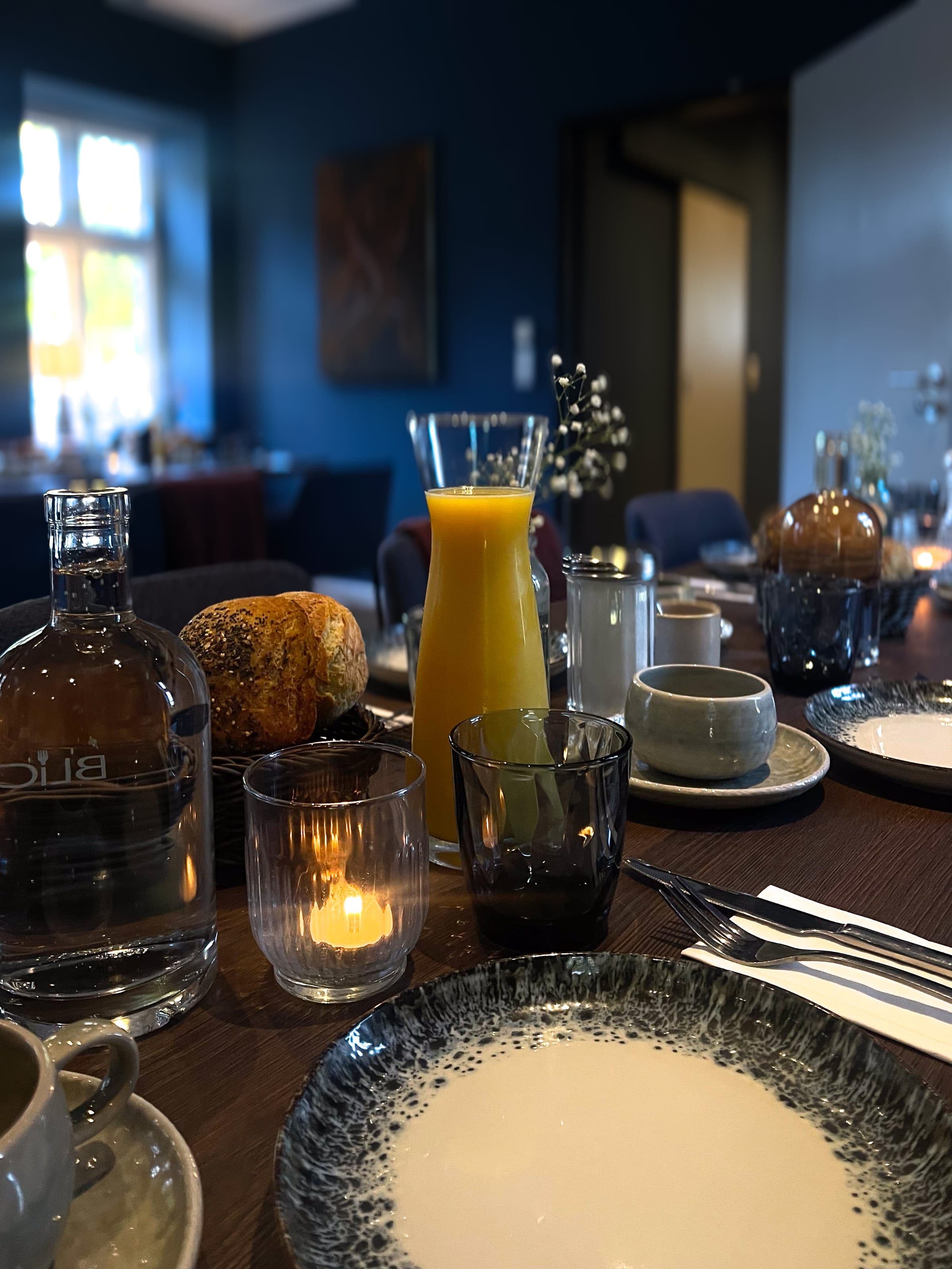 Frühstückstisch — Gedeckter Frühstückstisch im BLICKFANG Eckernförde mit Orangensaft-Karaffe, Brot und Kerze — blaue Wand und Sitzbereich